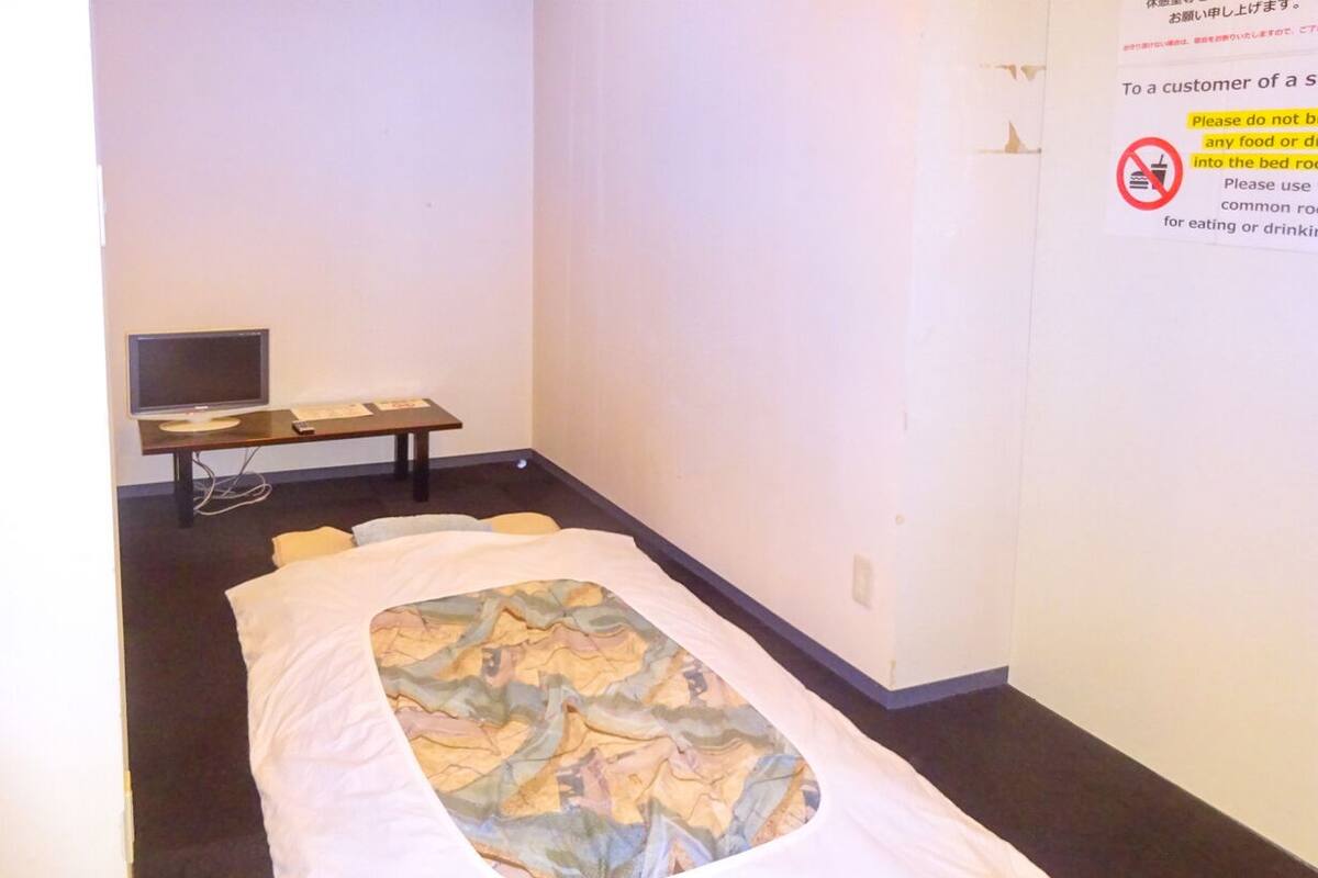 A single bed with a patterned bedspread, a bedside table with a lamp, and a wall-mounted TV.