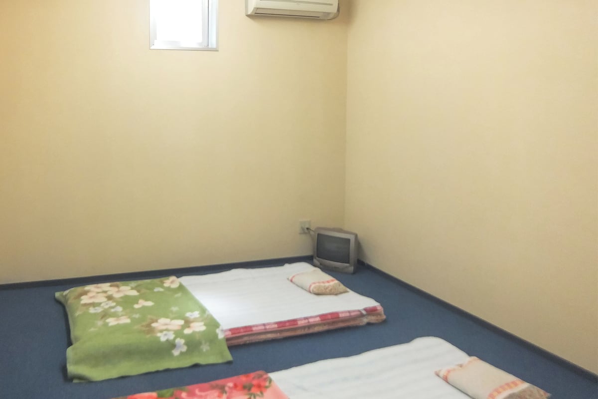 A small room with two beds, a window, an air conditioner, and a television.