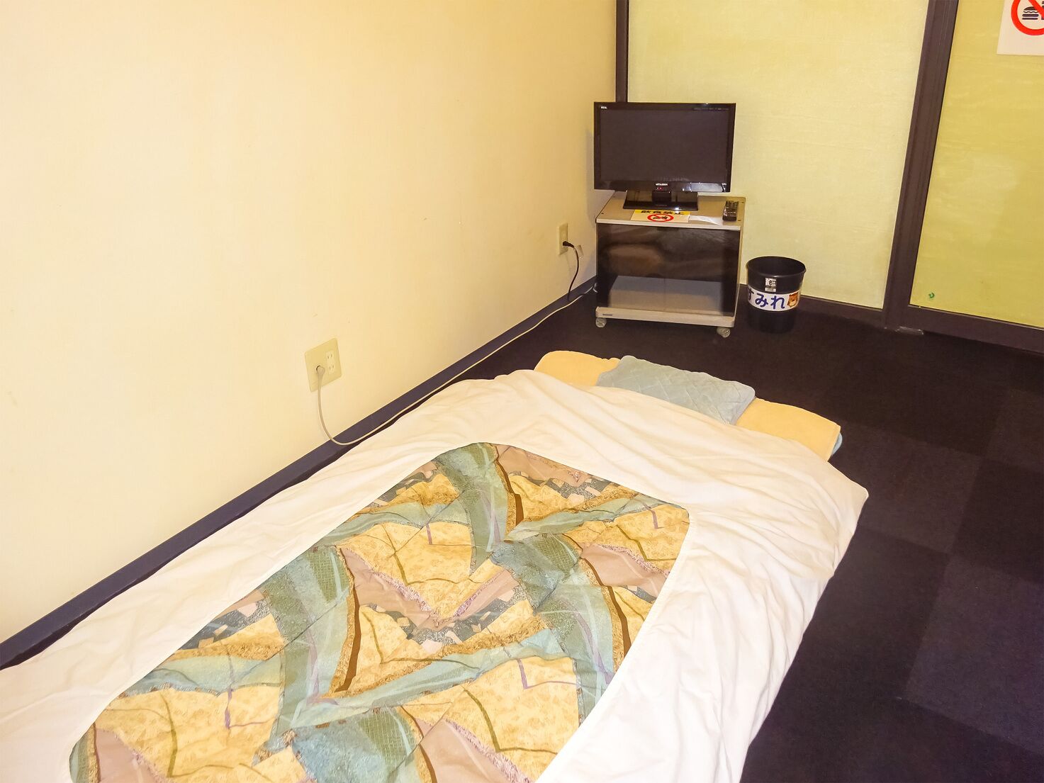 Habitación de hotel con una cama, televisión sobre un mueble, un cubo de basura y un enchufe en la pared.