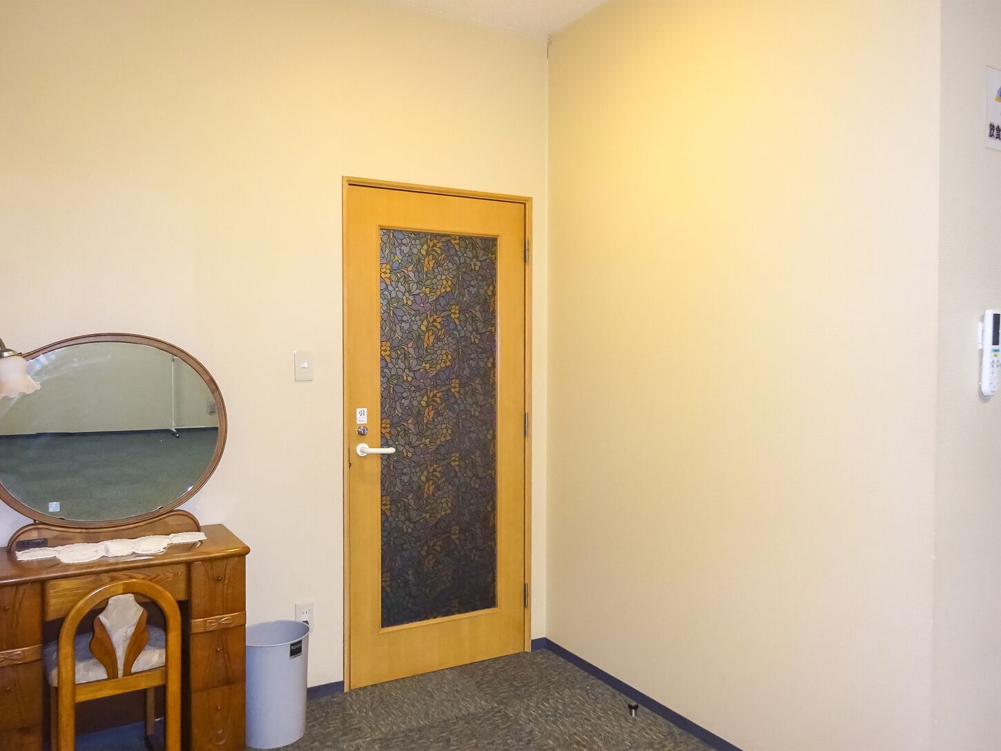 Una habitación con una puerta de madera, un espejo, un aparador de madera y un cubo de basura.