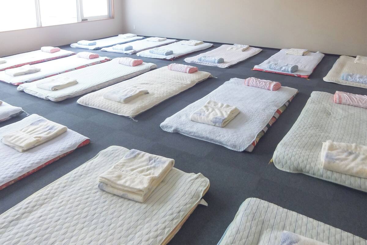 A room with multiple beds arranged in rows, each with a neatly folded blanket and pillow.