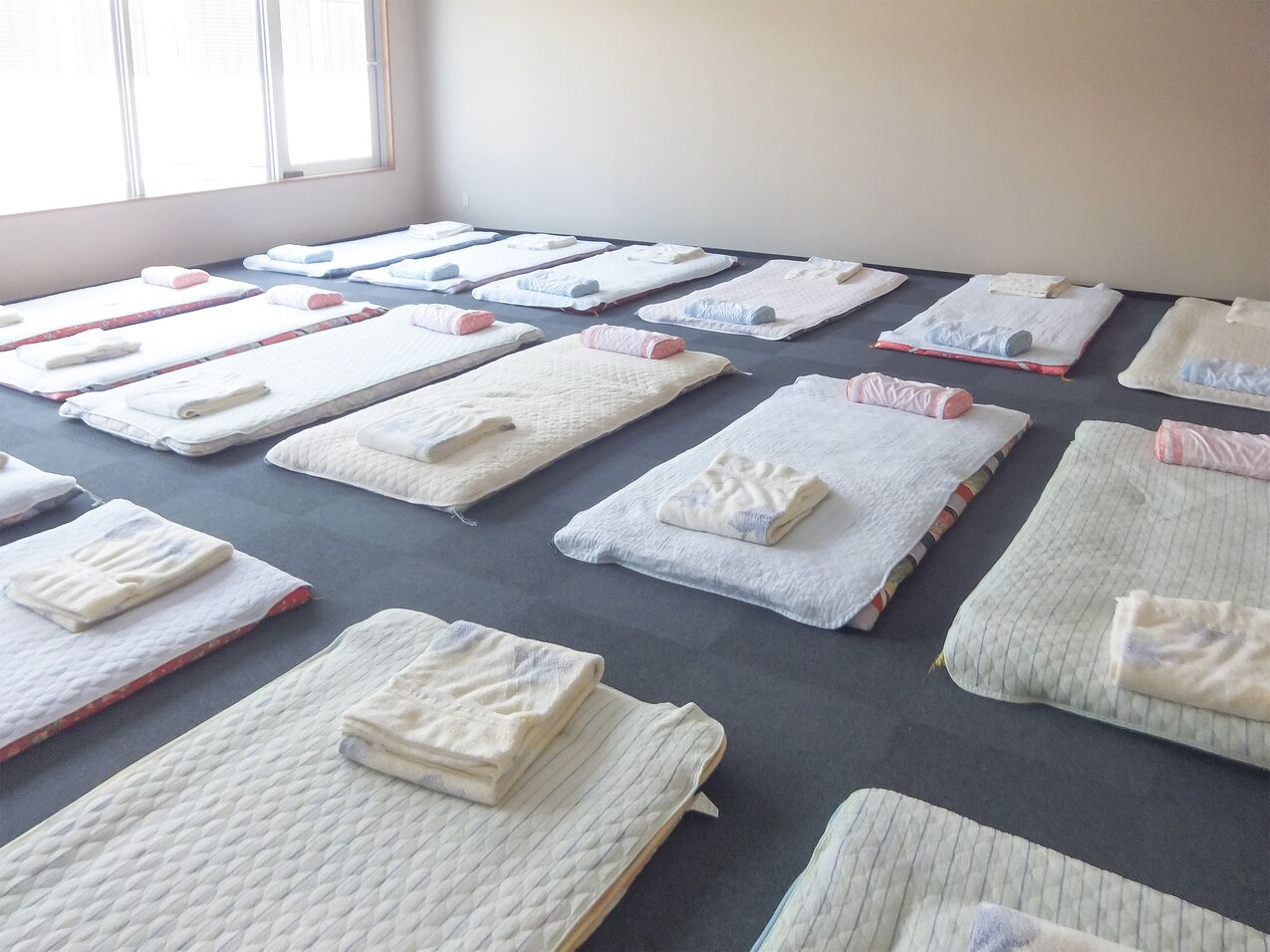 A room with multiple beds arranged in rows, each with a neatly folded blanket and pillow.