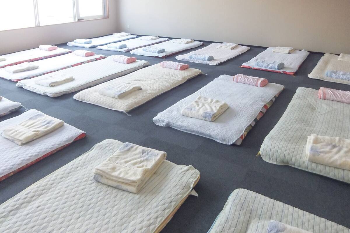 A room with multiple beds arranged in rows, each with a neatly folded blanket and pillow.