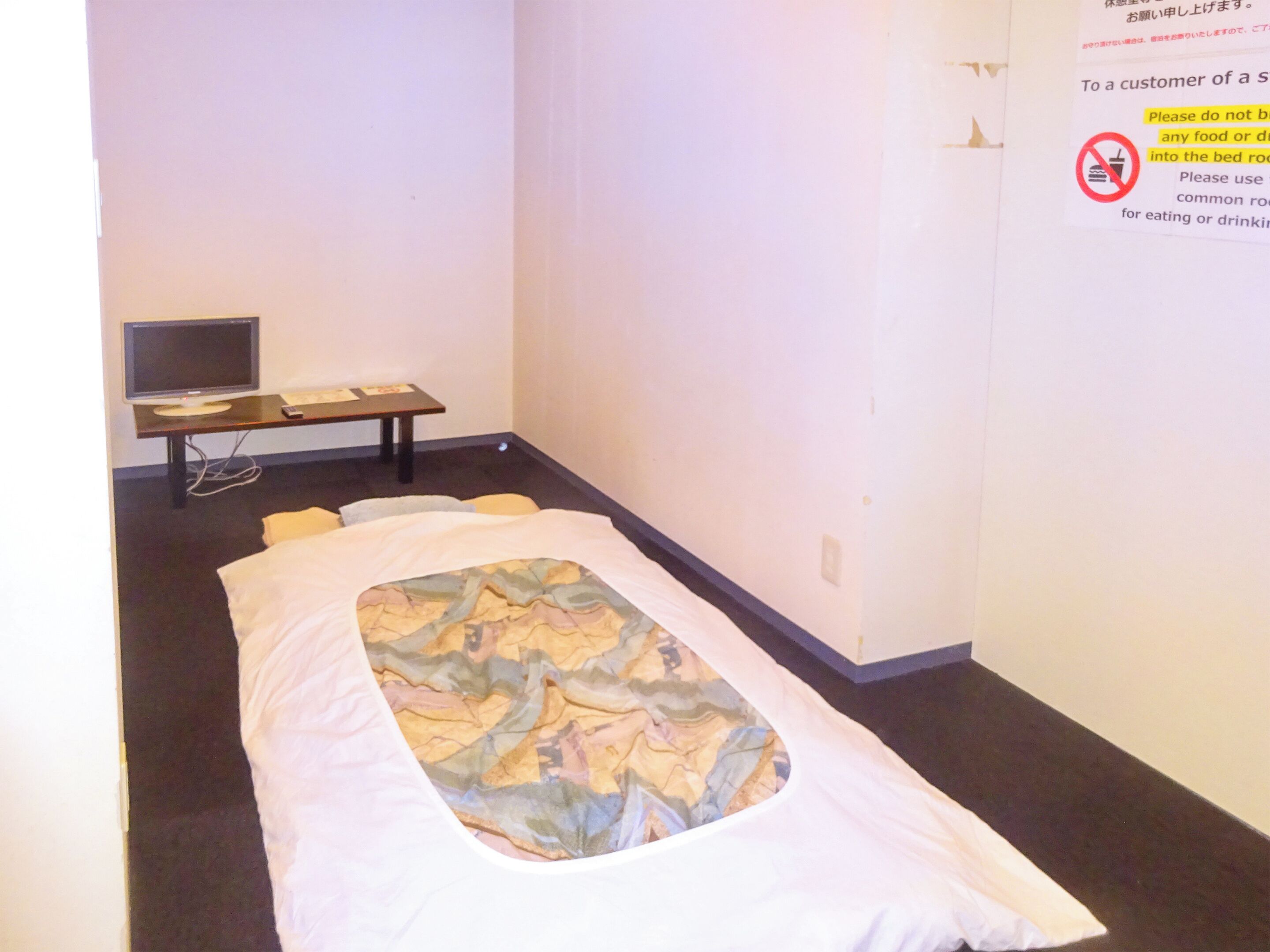 Una cama individual con una colcha estampada, una mesita de noche con lámpara y un televisor sobre un mueble.