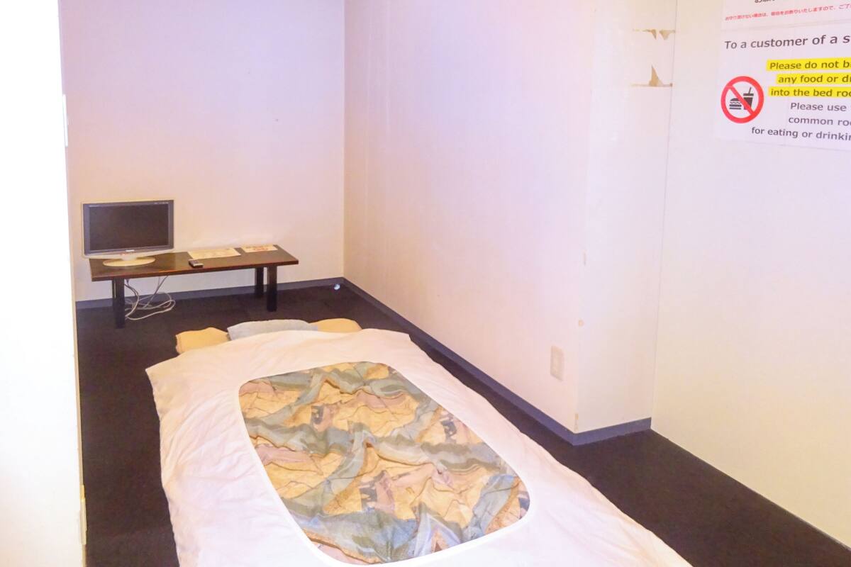 A single bed with a patterned bedspread, a bedside table with a lamp, and a television on a stand.