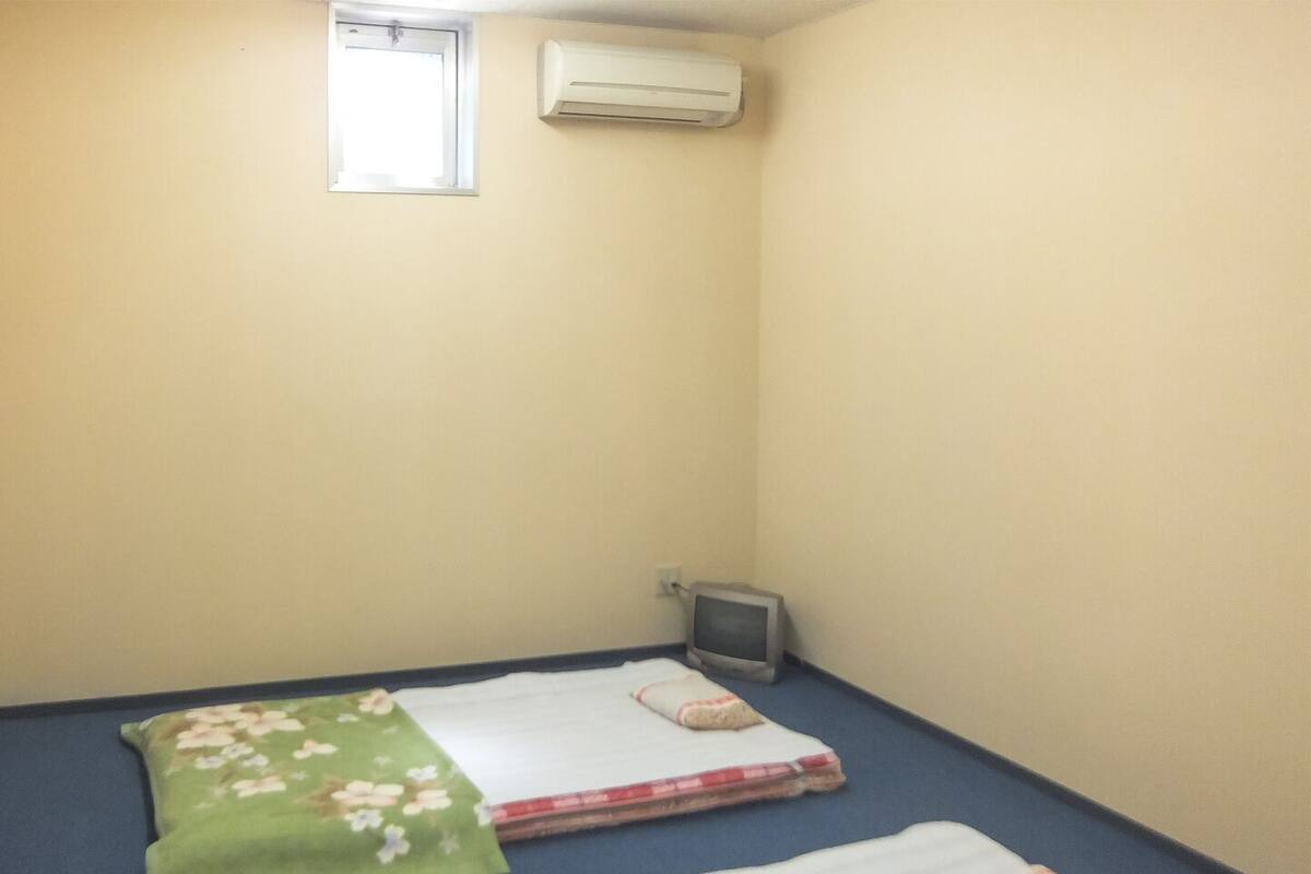 A small room with two beds, a window, and an air conditioning unit.
