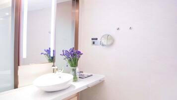 A modern bathroom with a white sink, a large mirror, and a vase with purple flowers.