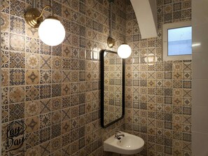 A bathroom with patterned tiles, a white sink, and two wall-mounted lights.