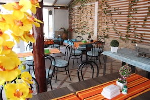 Un comedor con pared de ladrillo, listones de madera y piso de baldosas. Hay mesas y sillas dispuestas para comer.
