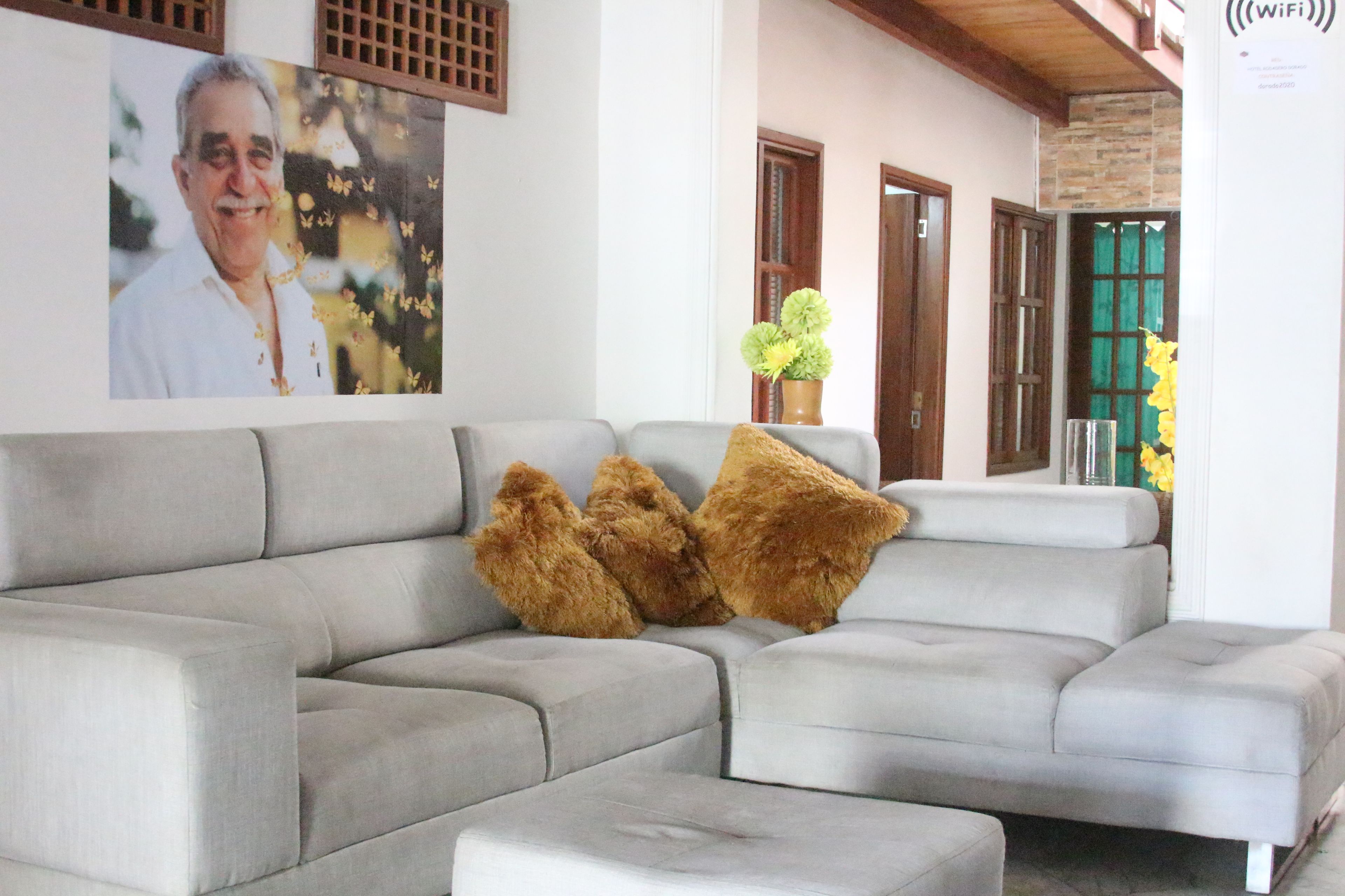 A living room with a grey sectional sofa, two brown furry throw pillows, a vase with green flowers, and a wall-mounted WiFi sign.