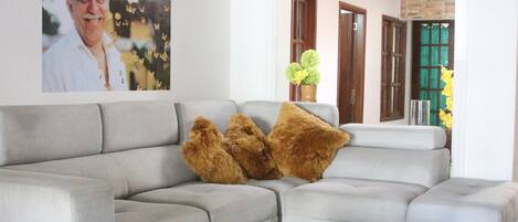 A living room with a grey sectional sofa, two brown furry throw pillows, a vase with green flowers, and a wall-mounted WiFi sign.