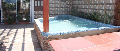 A hot tub in a tiled outdoor area with a pergola overhead.