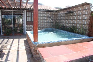 A hot tub in a tiled outdoor area with a pergola overhead.