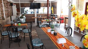 A restaurant with multiple tables and chairs, a television mounted on the wall, and a variety of plants and flowers.