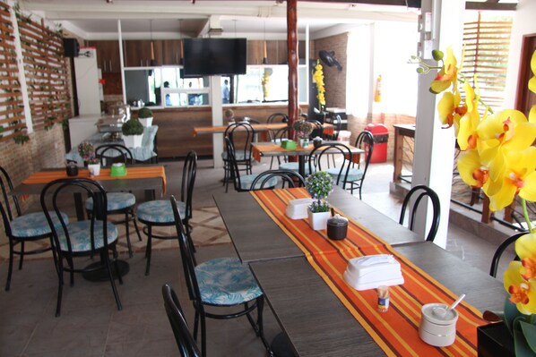 Un restaurante con varias mesas y sillas, un televisor montado en la pared y una variedad de plantas y flores.
