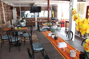 A restaurant with multiple tables and chairs, a television mounted on the wall, and a variety of plants and flowers. - Rodadero Dorado (Santa Marta)