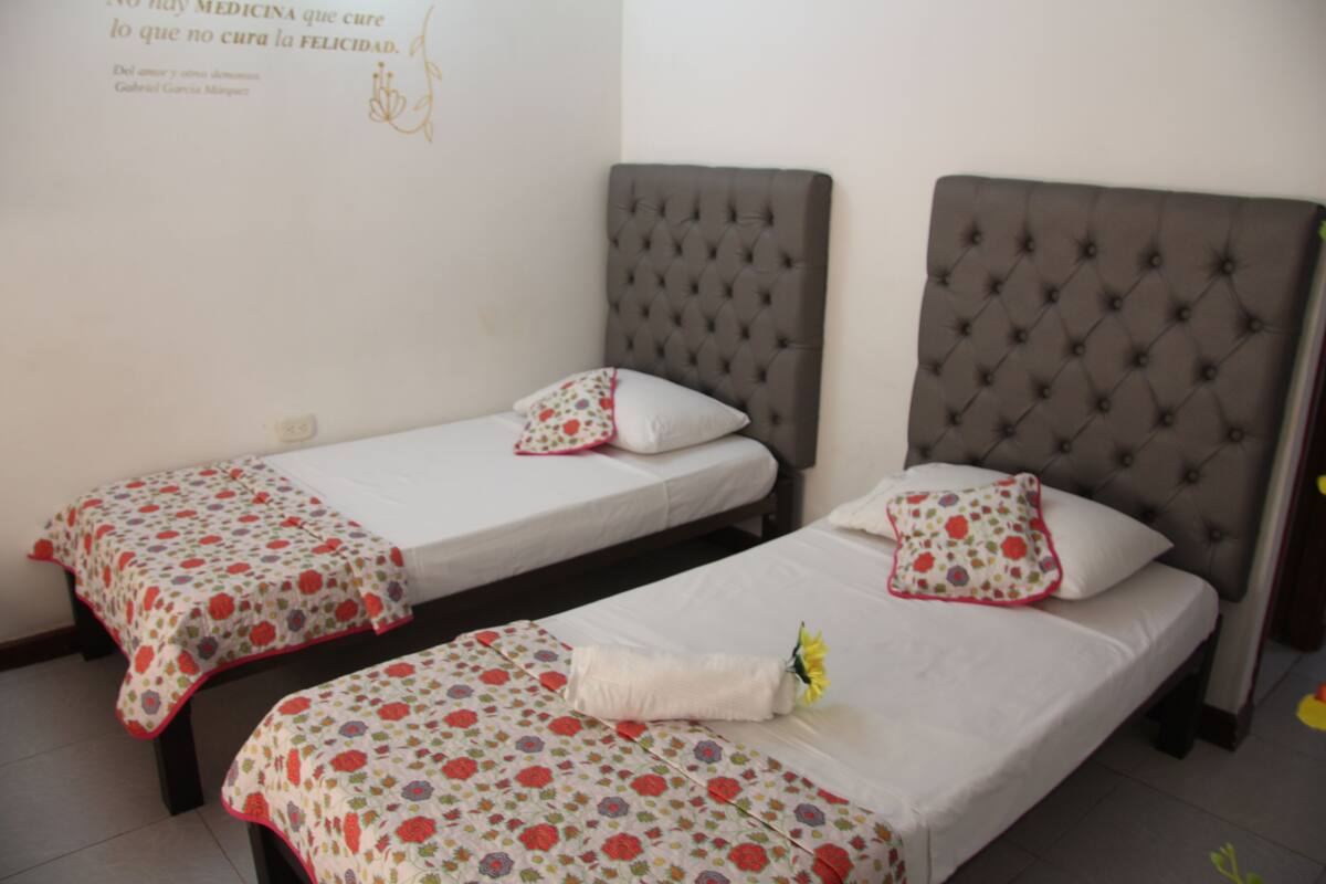 Two single beds with floral-patterned bedding, a tufted headboard, and a wall with a decorative quote.