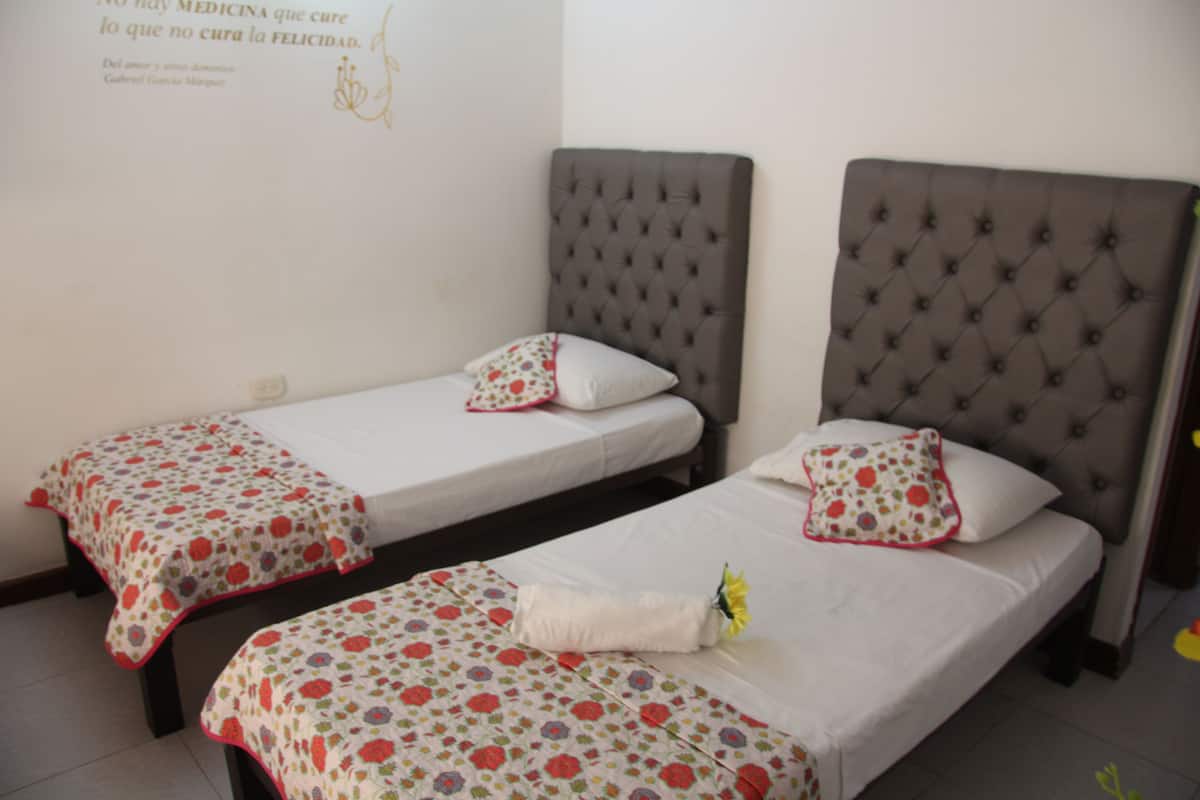Dos camas individuales con ropa de cama estampada con motivos florales, un cabecero capitonado y una pared con una cita decorativa.