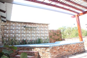 An outdoor patio area with a brick wall, a metal grill, and a wooden pergola. - Rodadero Dorado (Santa Marta)