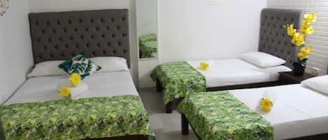 A hotel room with three beds, each with a green floral bedspread and a single yellow flower.