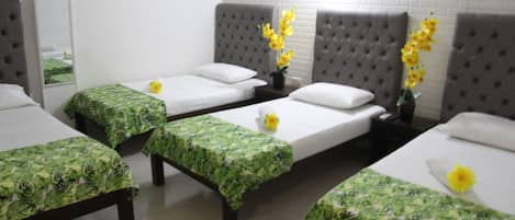 A hotel room with three single beds, each with a green floral bedspread, a mirror, and a wall with a white brick pattern.
