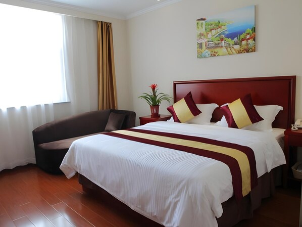 Una habitación de hotel con cama, una silla, una mesita de noche, una planta en maceta y un cuadro en la pared.
