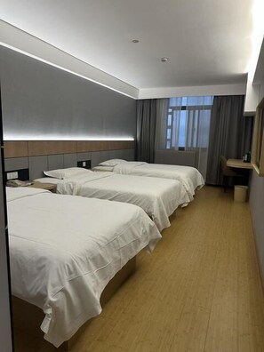 A hotel room with three beds, a desk, and a window with curtains.