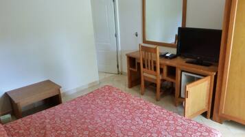 Ein Zimmer mit einem Bett, einem Schreibtisch mit Stuhl, einem Fernseher und einem kleinen Schrank.