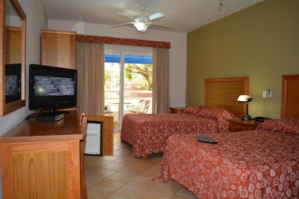 A hotel room with a television, two beds with patterned bedding, a ceiling fan, and a view of the outdoors. - New Garden Hotel (Sosúa)