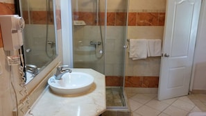 A bathroom with a sink, mirror, glass shower enclosure, and a door. - New Garden Hotel (Sosúa)