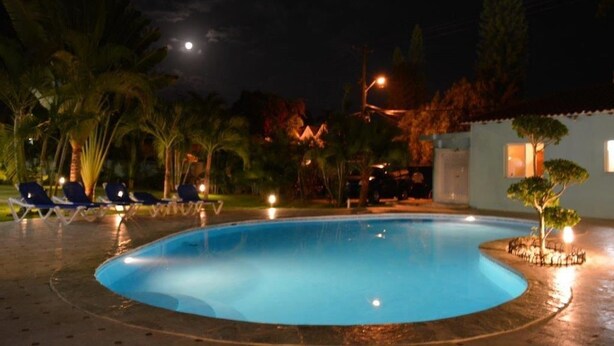A swimming pool at night with surrounding lounge chairs and a small building.