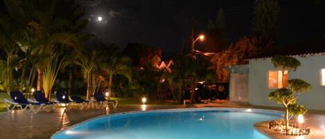 A nighttime pool area with lounge chairs and a small building in the background.