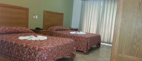 A hotel room with two beds, each with patterned bedding and towels. There is a nightstand with a phone and a wall-mounted thermostat.