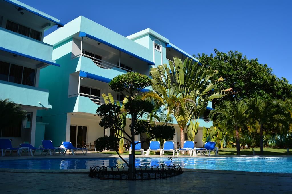 A hotel with a pool area, blue lounge chairs, and palm trees.