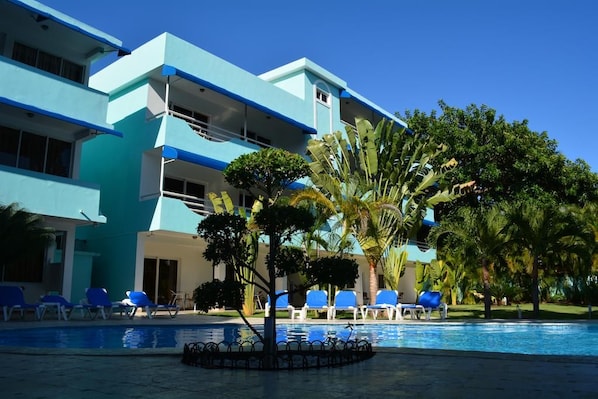 A hotel with a pool area, blue lounge chairs, and palm trees. - New Garden Hotel (Sosúa)