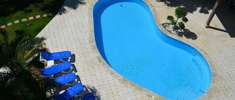 A swimming pool with a curved edge, surrounded by a tiled deck with a dotted pattern.