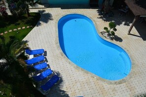 A swimming pool with a curved edge, surrounded by a tiled deck with a dotted pattern. - New Garden Hotel (Sosúa)