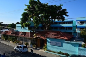 A hotel with a blue facade, a red-tiled roof, and a sign reading "New Garden Hotel." - New Garden Hotel (Sosúa)