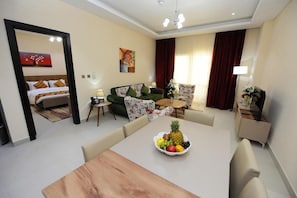 A hotel room with a bed, a sofa, a dining table with fruit, and a view of the outside. - Al Mansour Park Inn Hotel Apartment (Doha)