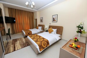 A hotel room with two beds, a TV, a desk with a fruit bowl, and a flower arrangement. - Al Mansour Park Inn Hotel Apartment (Doha)