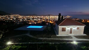 A small stone house with a tiled roof, a swimming pool, and a view of a lit-up town in the background. - Uphill Glavanovic Villa (Bar)
