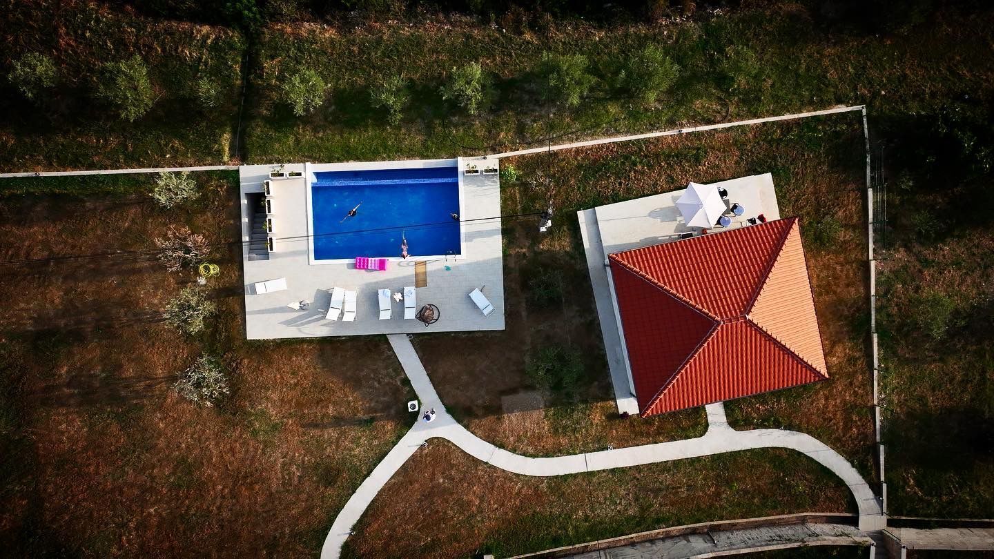 Vista aérea de uma propriedade com piscina, estrutura com telhado vermelho e caminho pavimentado.