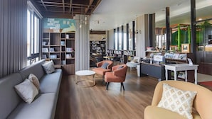 A modern library with a sofa, chairs, and bookshelves. - Senyum World Hotel (Batu)