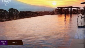 A serene pool area at sunset with a view of distant mountains, a covered seating area, and a clear sky. - Senyum World Hotel (Batu)