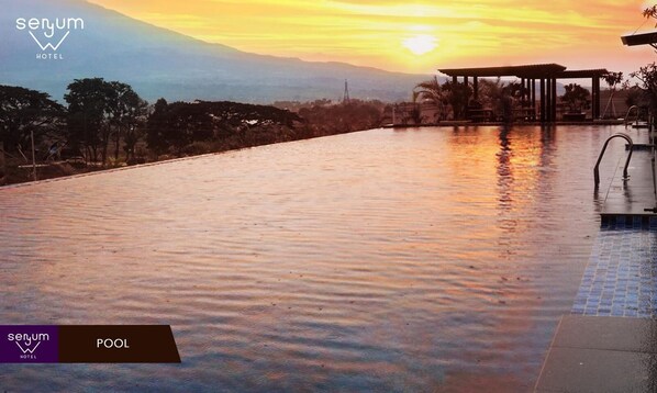 A serene pool area at sunset with a view of distant mountains, a covered seating area, and a clear sky.