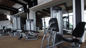 A gym with various exercise machines, large windows, and a high ceiling. - Senyum World Hotel (Batu)