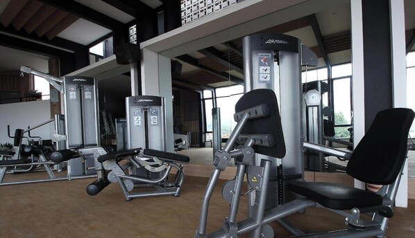 A gym with various exercise machines, large windows, and a high ceiling.