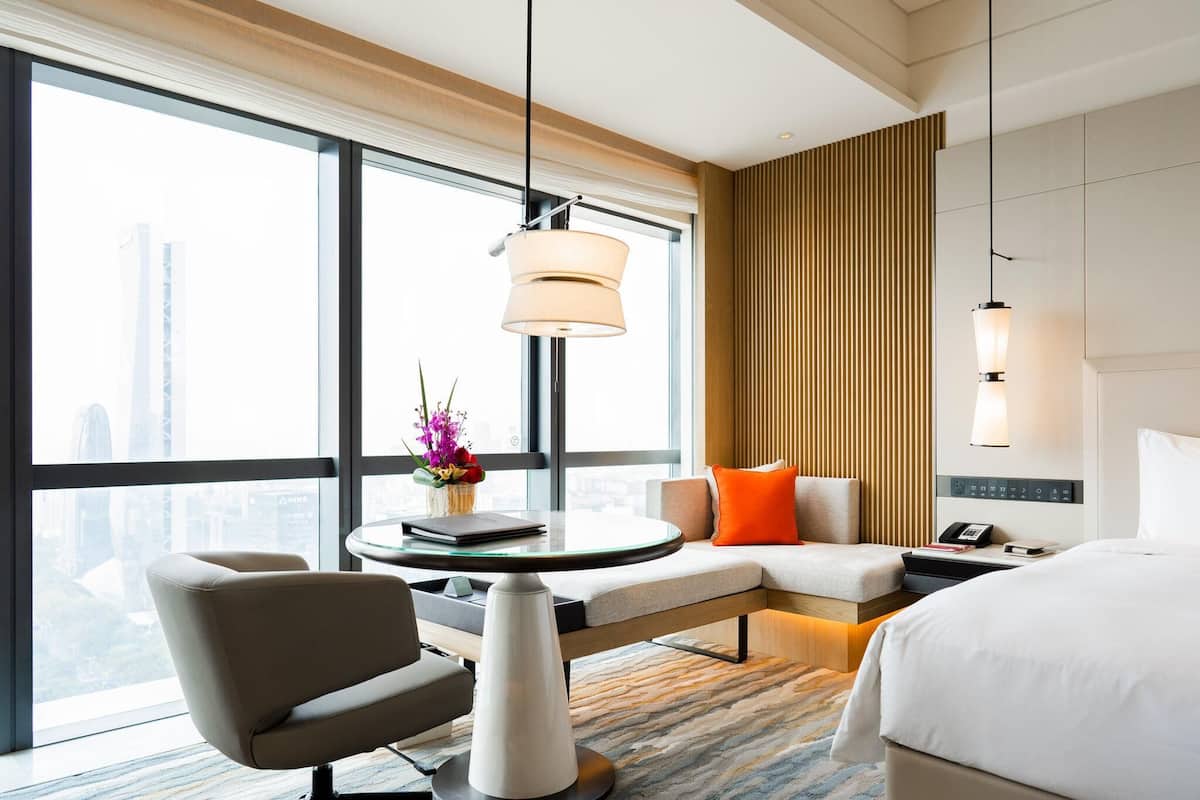 Quarto de hotel moderno com uma grande janela, uma mesa redonda, um sofá e uma cama.
