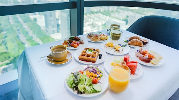 A table with breakfast items including waffles, croissants, and various fruits, set against a city view. - Crowne Plaza Shenzhen Nanshan (Shenzhen)