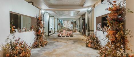 Un pasillo con un arreglo floral central, flanqueado por paredes con cuadros enmarcados y plantas decorativas.